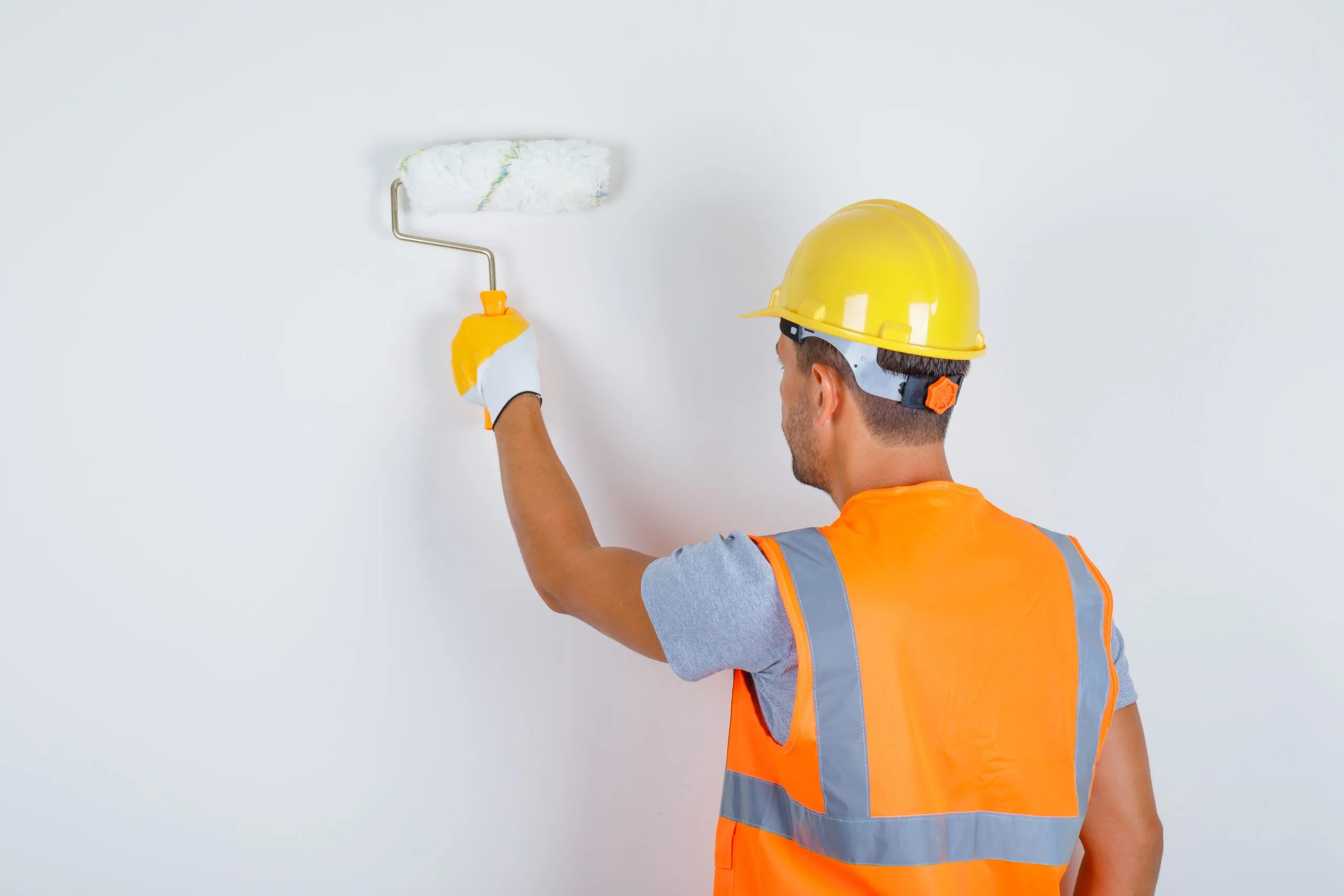 Male builder uniform helmet gloves painting wall with roller back view