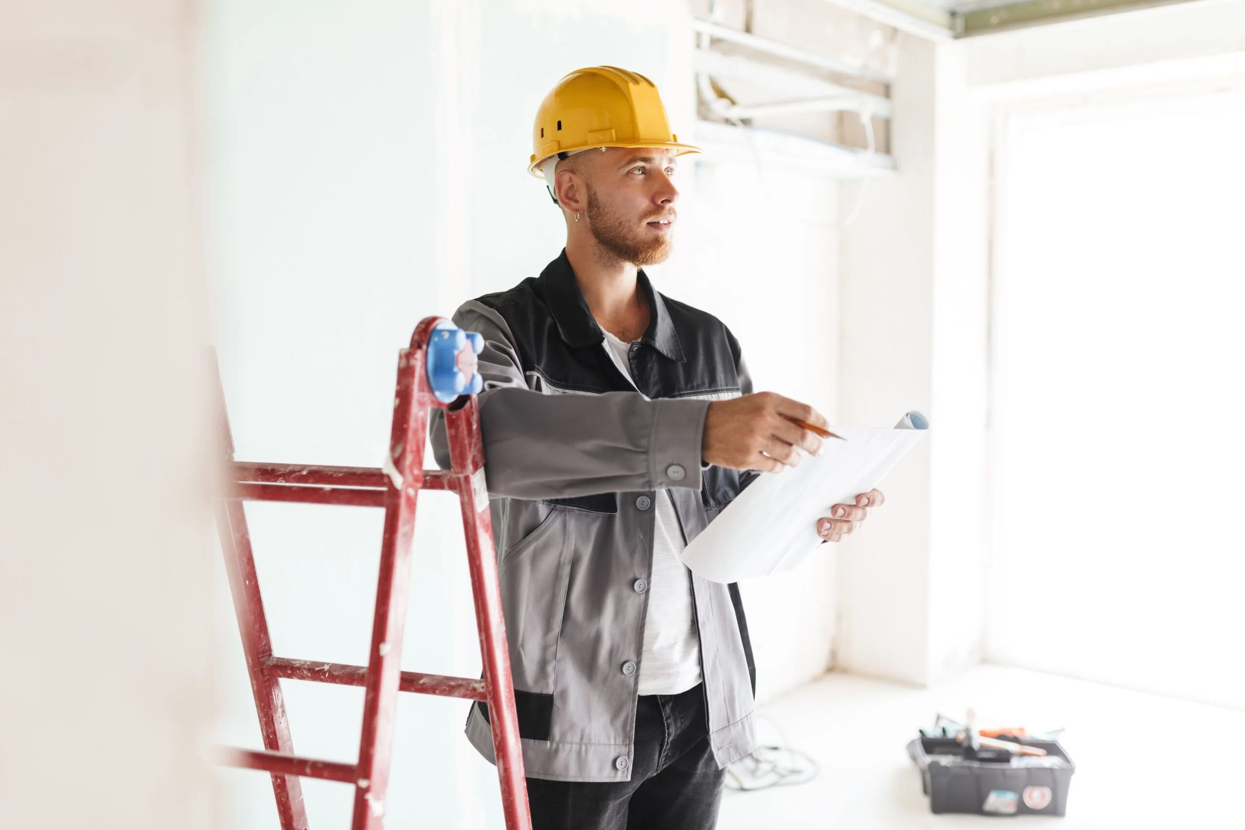 Young engineer in work clothes and a yellow hard hat holding tools