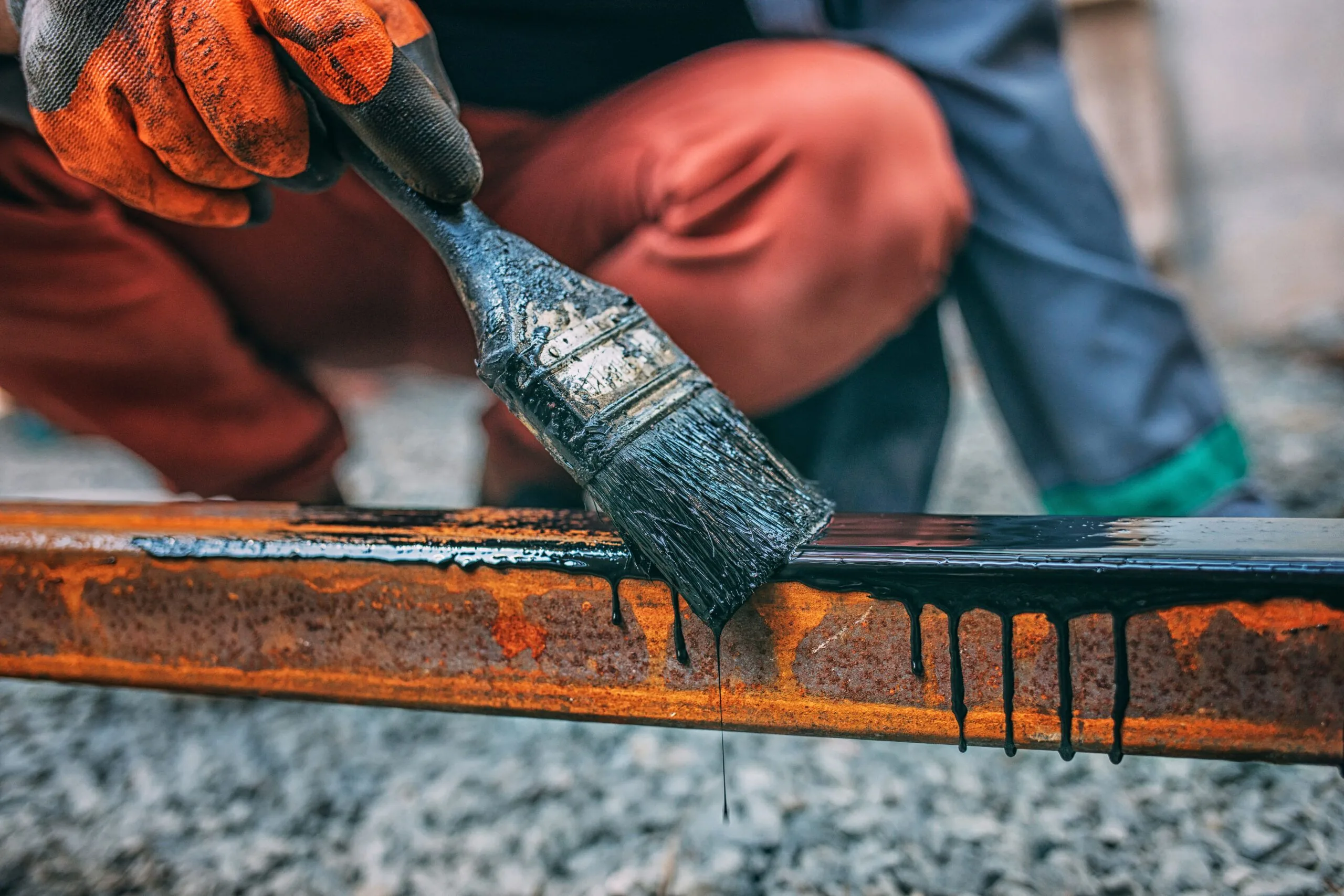 Man hand paints metal post with brush with black paint